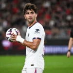Een PSG-speler in wit tijdens een wedstrijdmoment met de bal in de handen.