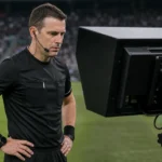Een scheidsrechter bekijkt een VAR-monitor naast de zijlijn tijdens een voetbalwedstrijd.