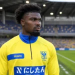 Loïc Mbe Soh in gele trainingskleding aan de rand van een voetbalveld.