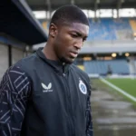Joel Ordoñez in een zwarte trainingsjas van Club Brugge naast het veld.
