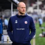 Arnaud Bodart in een donkerblauw trainingsjack langs het veld voor een wedstrijd.