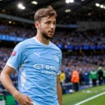 Nico González in lichtblauw Manchester City-tenue langs de rand van een voetbalveld.