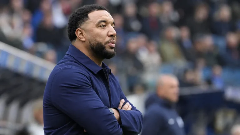 Troy Deeney kijkt aandachtig toe langs de zijlijn van een voetbalstadion.