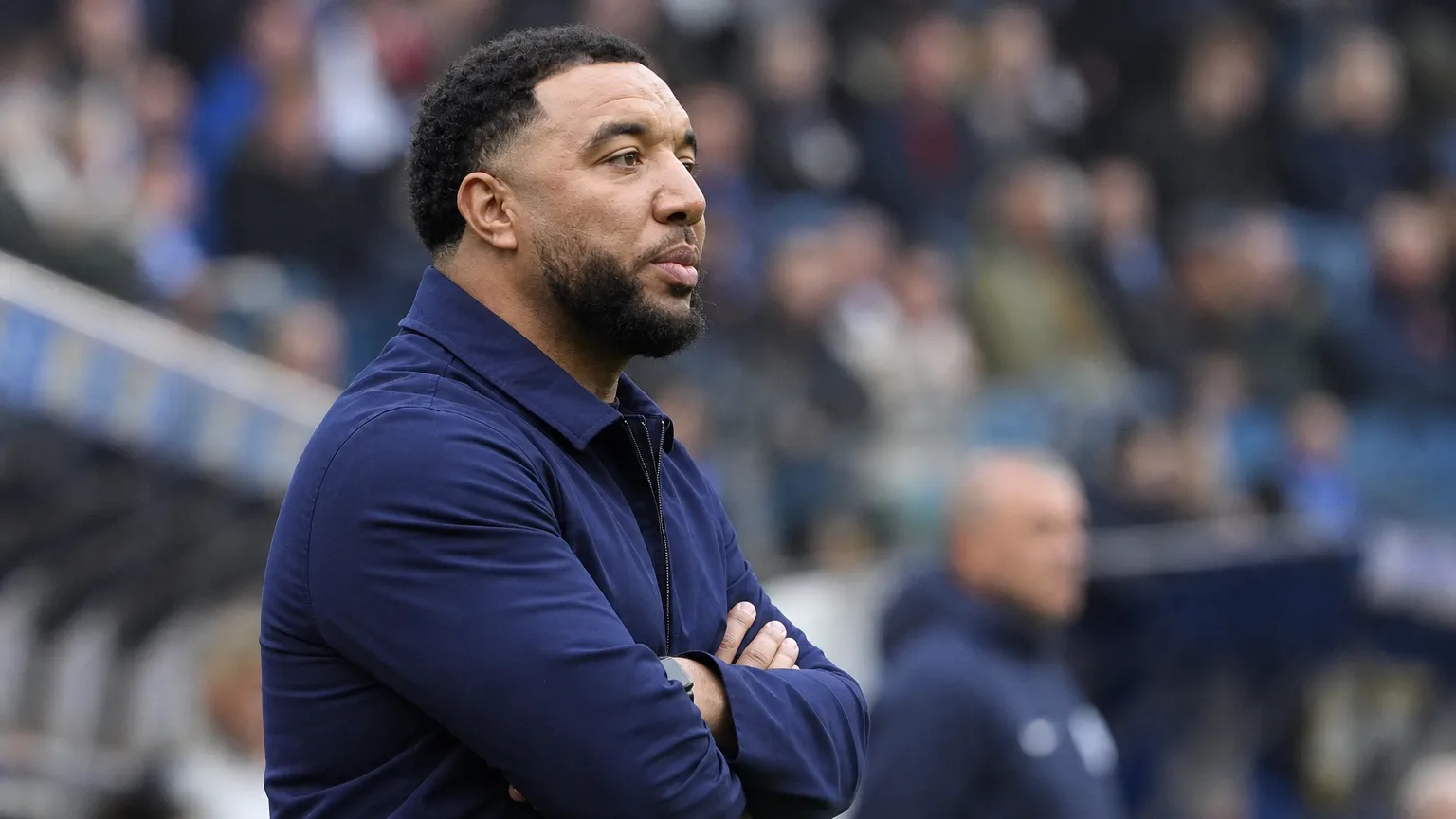 Troy Deeney kijkt aandachtig toe langs de zijlijn van een voetbalstadion.