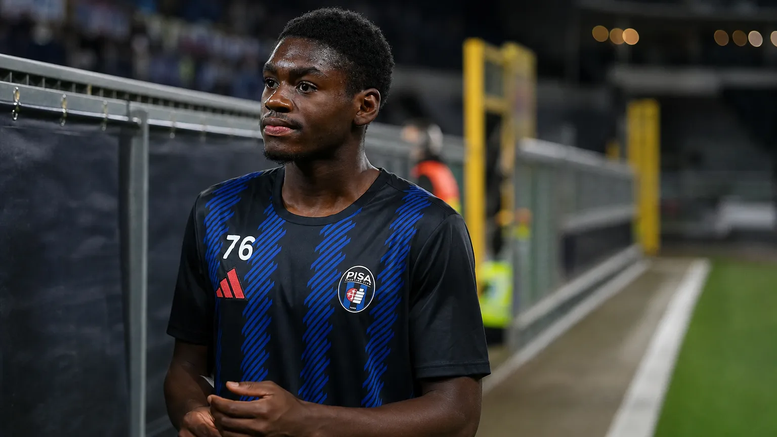 Jérémy Mbambi in zijn Pisa-tenue langs de rand van een stadionveld.