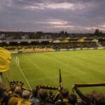Het Herman Vanderpoortenstadion in Lier domineert de scène, met geel-zwarte tribunes en supporters van K. Lierse SK.