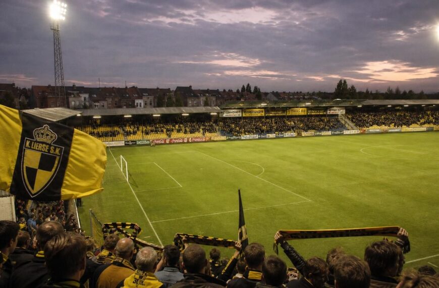 Het Herman Vanderpoortenstadion in Lier domineert de scรจne, met geel-zwarte tribunes en supporters van K. Lierse SK.