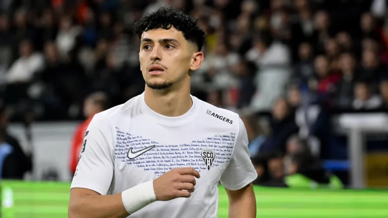 Yassin Belkhdim in een wit voetbalshirt aan de rand van het veld voor een wedstrijd.
