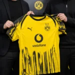 Niet-herkenbare clubvertegenwoordigers presenteren een Borussia Dortmund-shirt in een officiële mediaruimte.