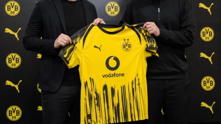 Niet-herkenbare clubvertegenwoordigers presenteren een Borussia Dortmund-shirt in een officiële mediaruimte.