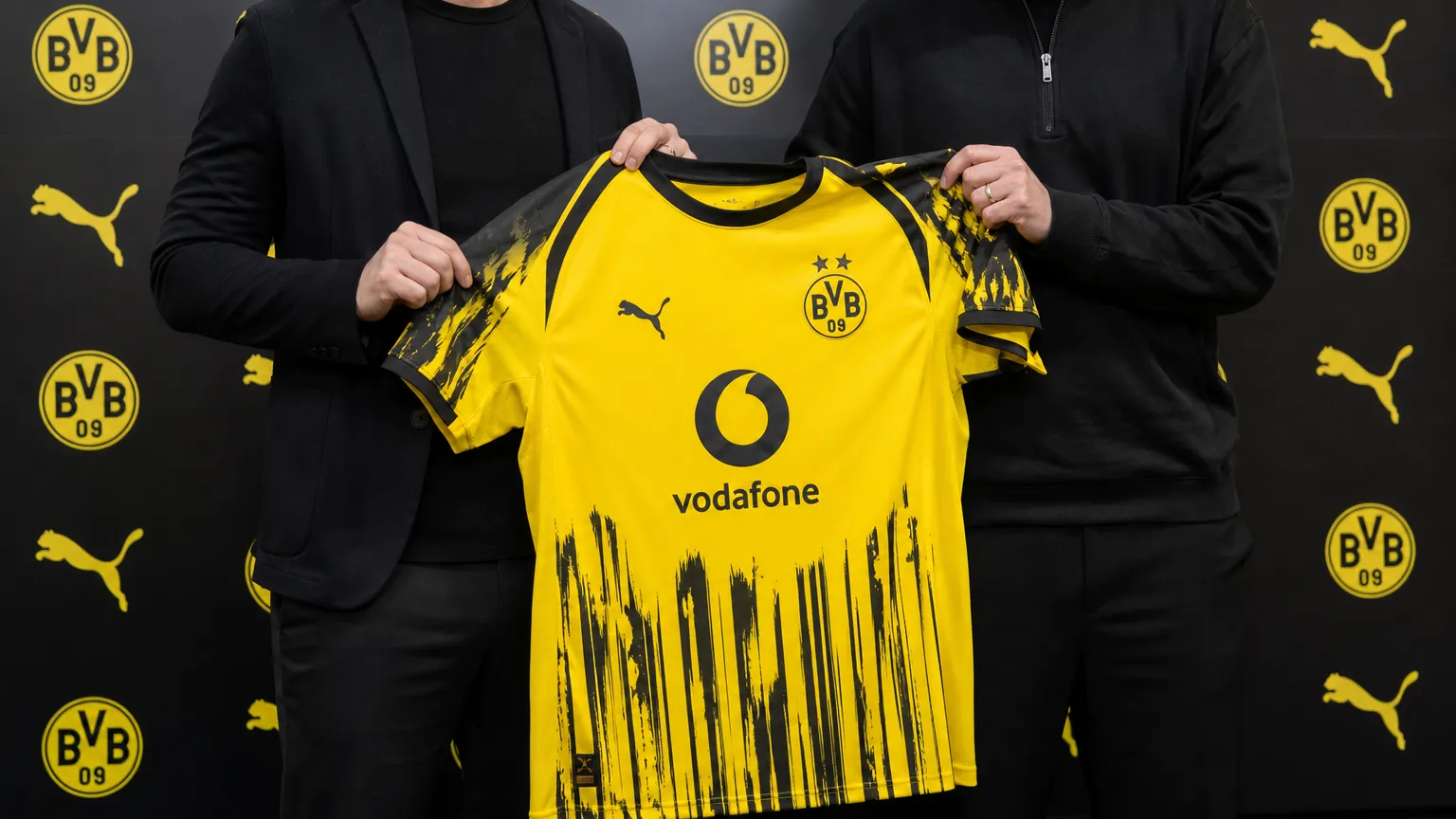 Niet-herkenbare clubvertegenwoordigers presenteren een Borussia Dortmund-shirt in een officiële mediaruimte.