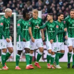 Een groep spelers in groen-witte tenues verzamelt zich vlak voor het doel.