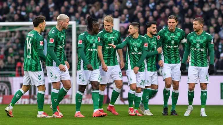 Een groep spelers in groen-witte tenues verzamelt zich vlak voor het doel.