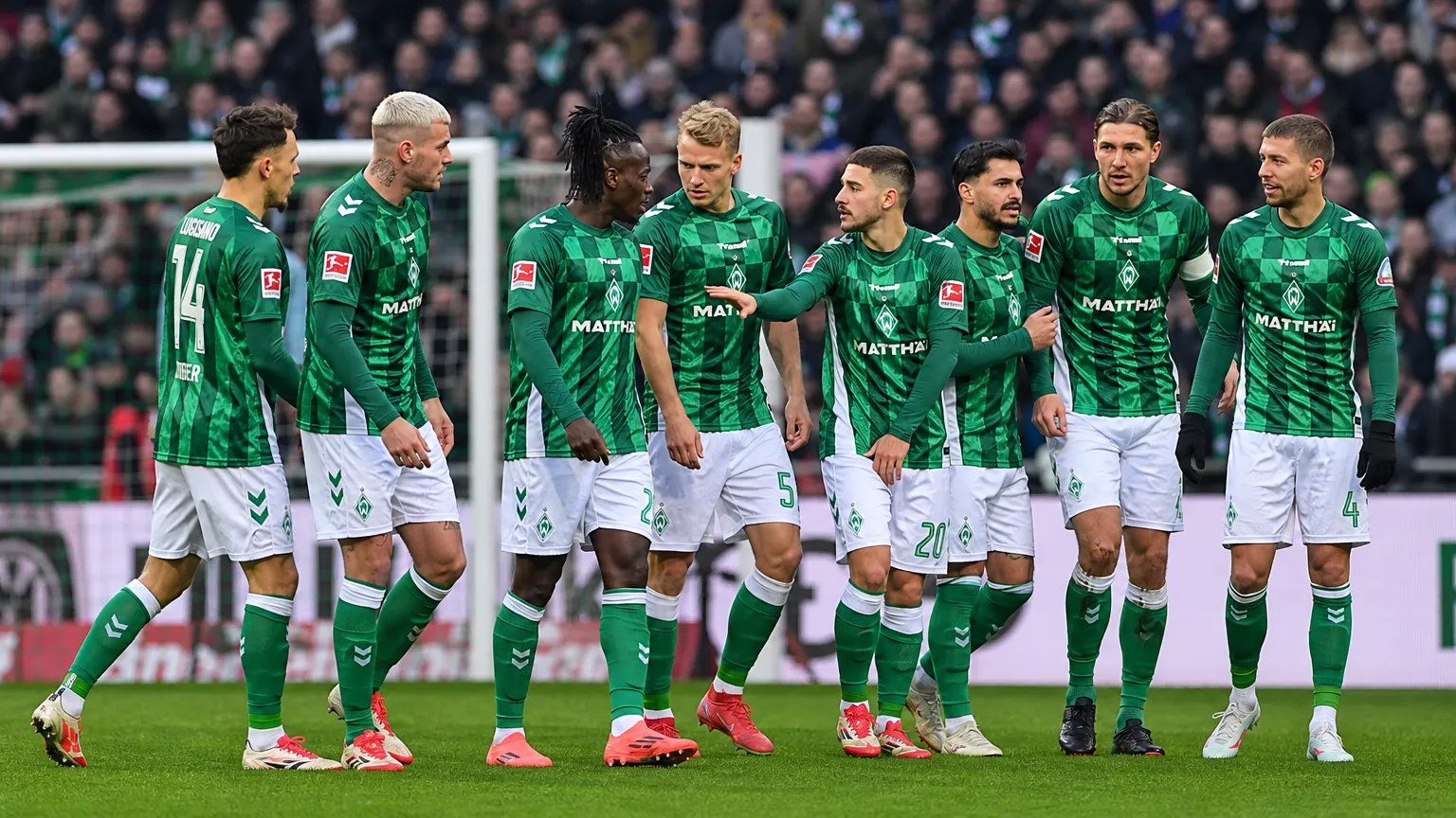 Een groep spelers in groen-witte tenues verzamelt zich vlak voor het doel.