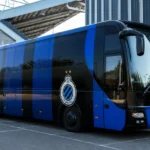 Een blauw-zwarte spelersbus van Club Brugge op een parkeerzone bij een voetbalstadion.