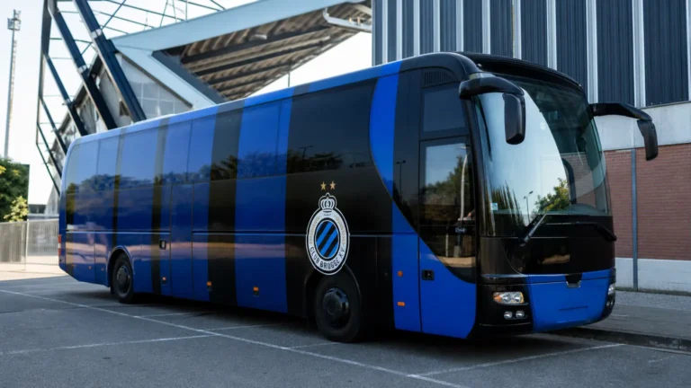 Een blauw-zwarte spelersbus van Club Brugge op een parkeerzone bij een voetbalstadion.