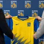 Niet-herkenbare clubvertegenwoordigers presenteren een KVC Westerlo-shirt in een officiële ruimte.