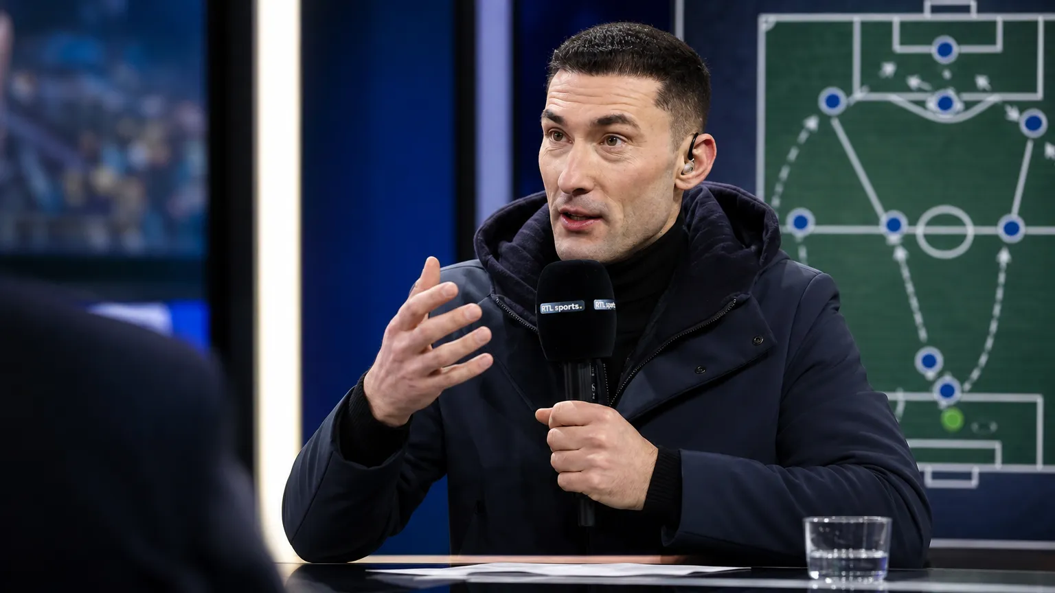Silvio Proto spreekt met een microfoon tijdens een voetbalanalyse in een televisiestudio.