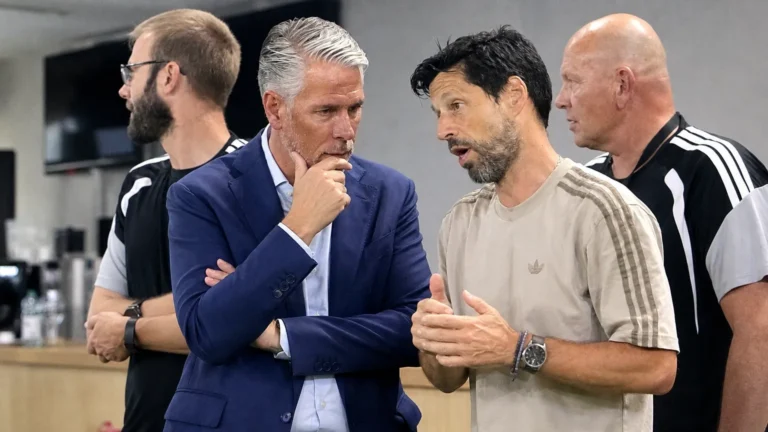 Vier clubmedewerkers in gesprek in een indoor voetbalomgeving.