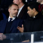 Een groep formeel geklede voetbalbestuurders overlegt in een stadiontribune.