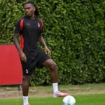 Rafael Leão in AC Milan-trainingskleding met een bal aan de rand van een voetbalveld.