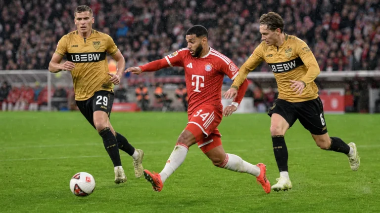 Een speler van Bayern München dribbelt met de bal terwijl twee spelers van Stuttgart achtervolgen.