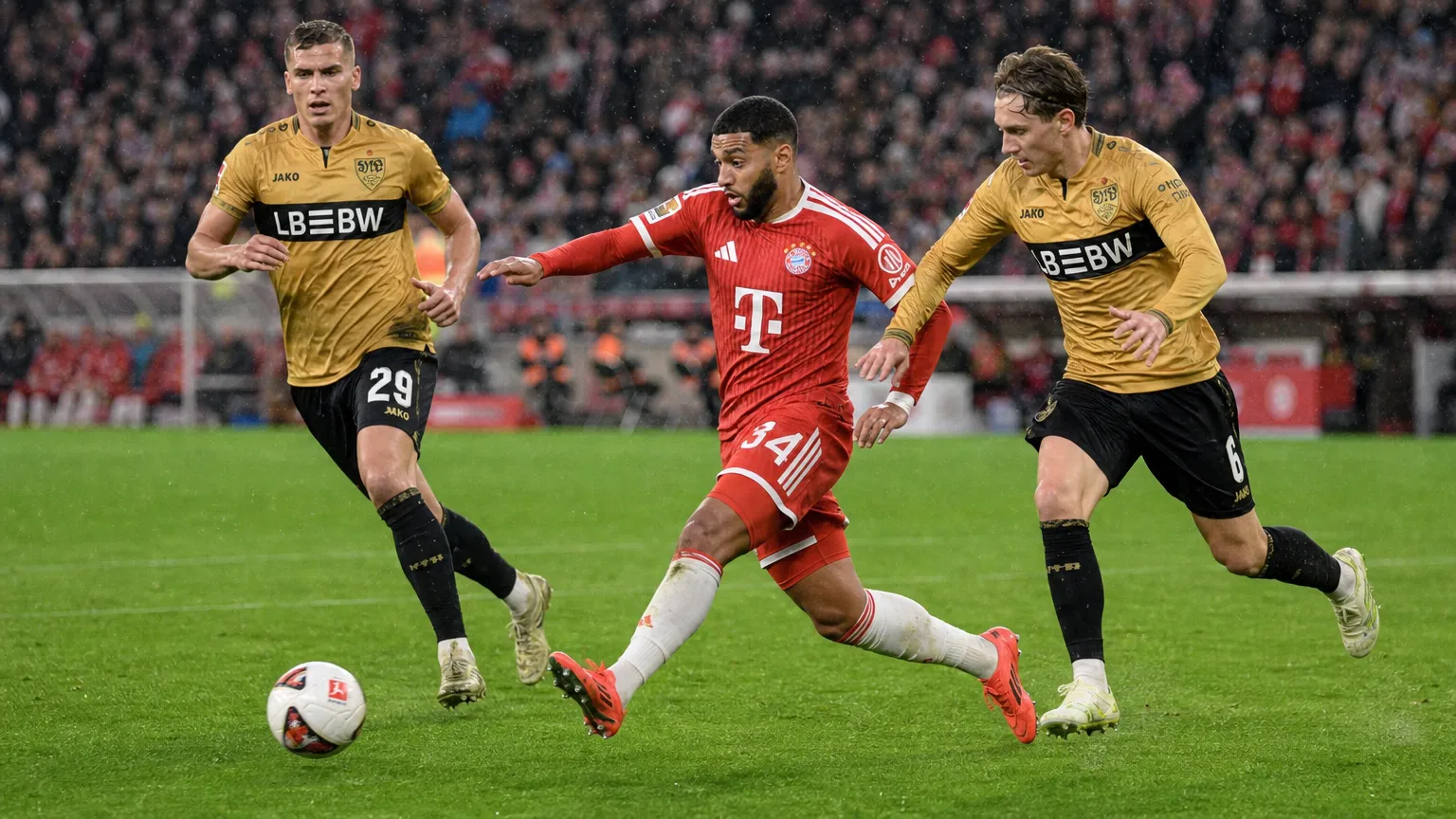 Een speler van Bayern München dribbelt met de bal terwijl twee spelers van Stuttgart achtervolgen.