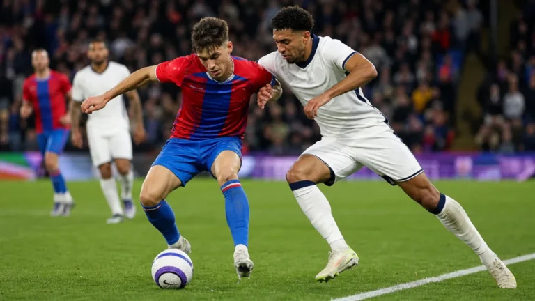 Twee voetballers vechten om de bal in het strafschopgebied tijdens een avondwedstrijd.