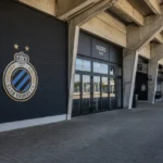 Een open stadionconcourse met een discreet Club Brugge-embleem aan een vaste wand.