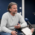 Rik De Mil spreekt in een KAA Gent-mediazaal met een discreet clublogo op de achtergrond.