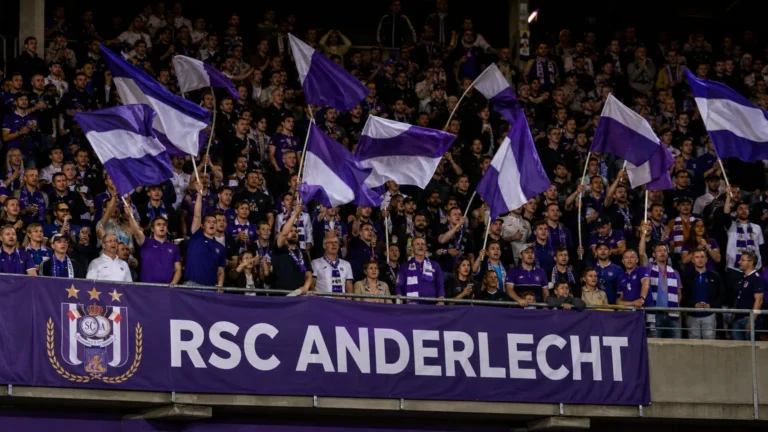 Anderlecht-supporters met paars-witte vlaggen in een volle tribune.