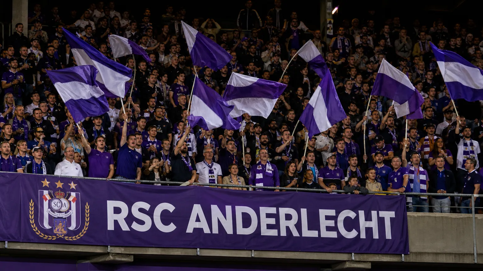 Anderlecht-supporters met paars-witte vlaggen in een volle tribune.