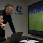 Medewerkers bekijken wedstrijdbeelden in een analyseruimte met een discreet KAA Gent-logo aan de muur.