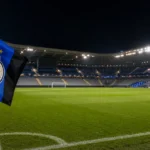 Een verlicht voetbalstadion met een Club Brugge-vlag langs het veld voor een Champions League-avond.