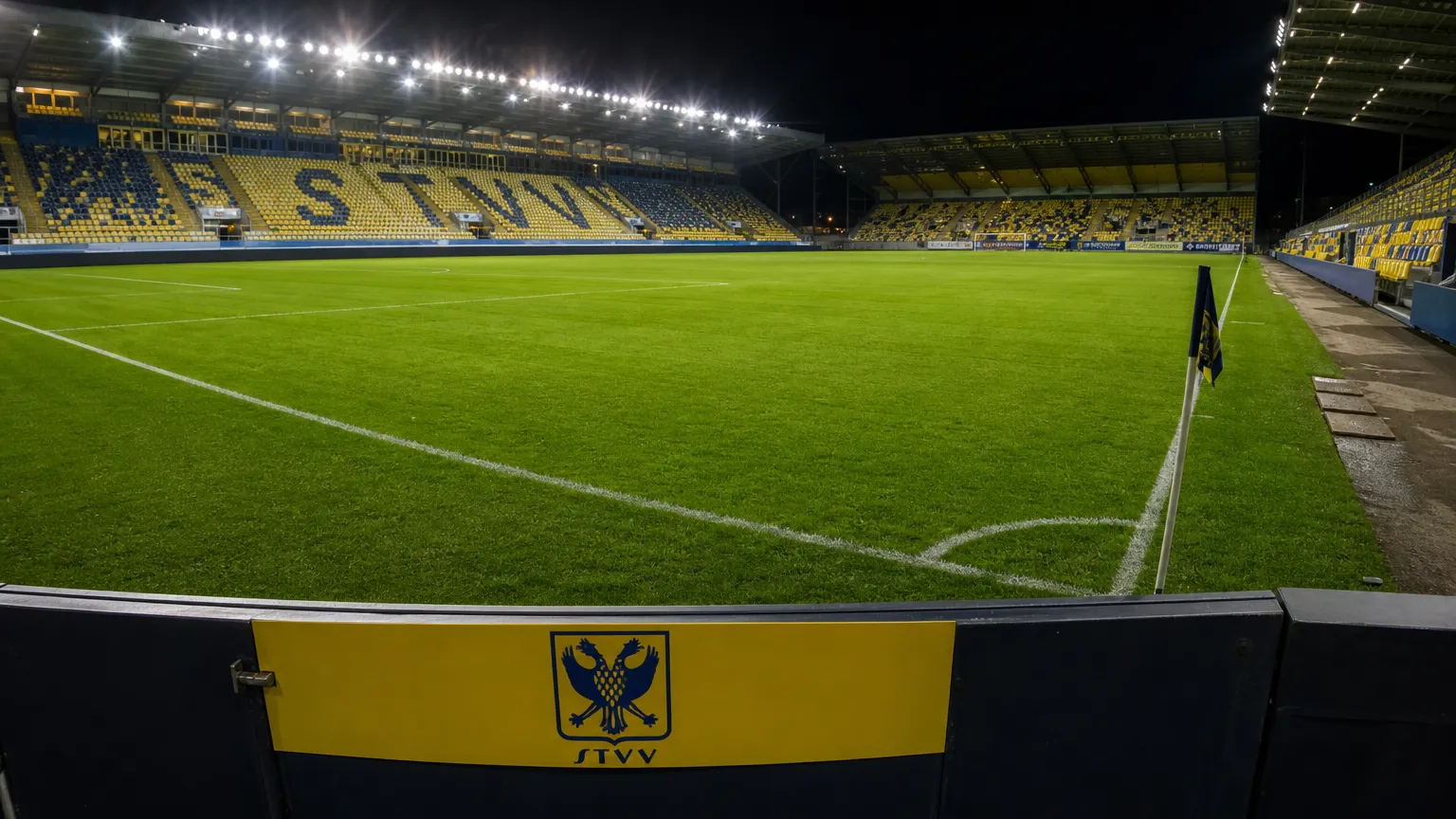 Verlicht veld in het stadion van STVV met een discreet clubbord.