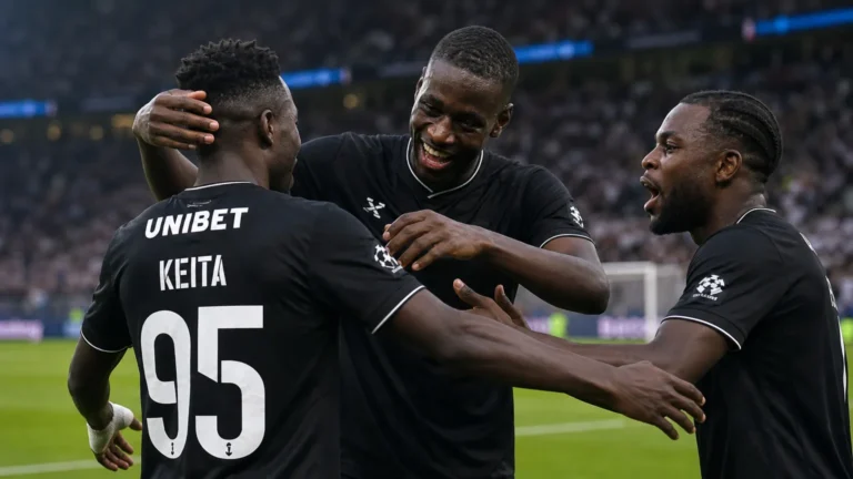 Drie spelers in zwarte wedstrijdtenues vieren samen op het veld.