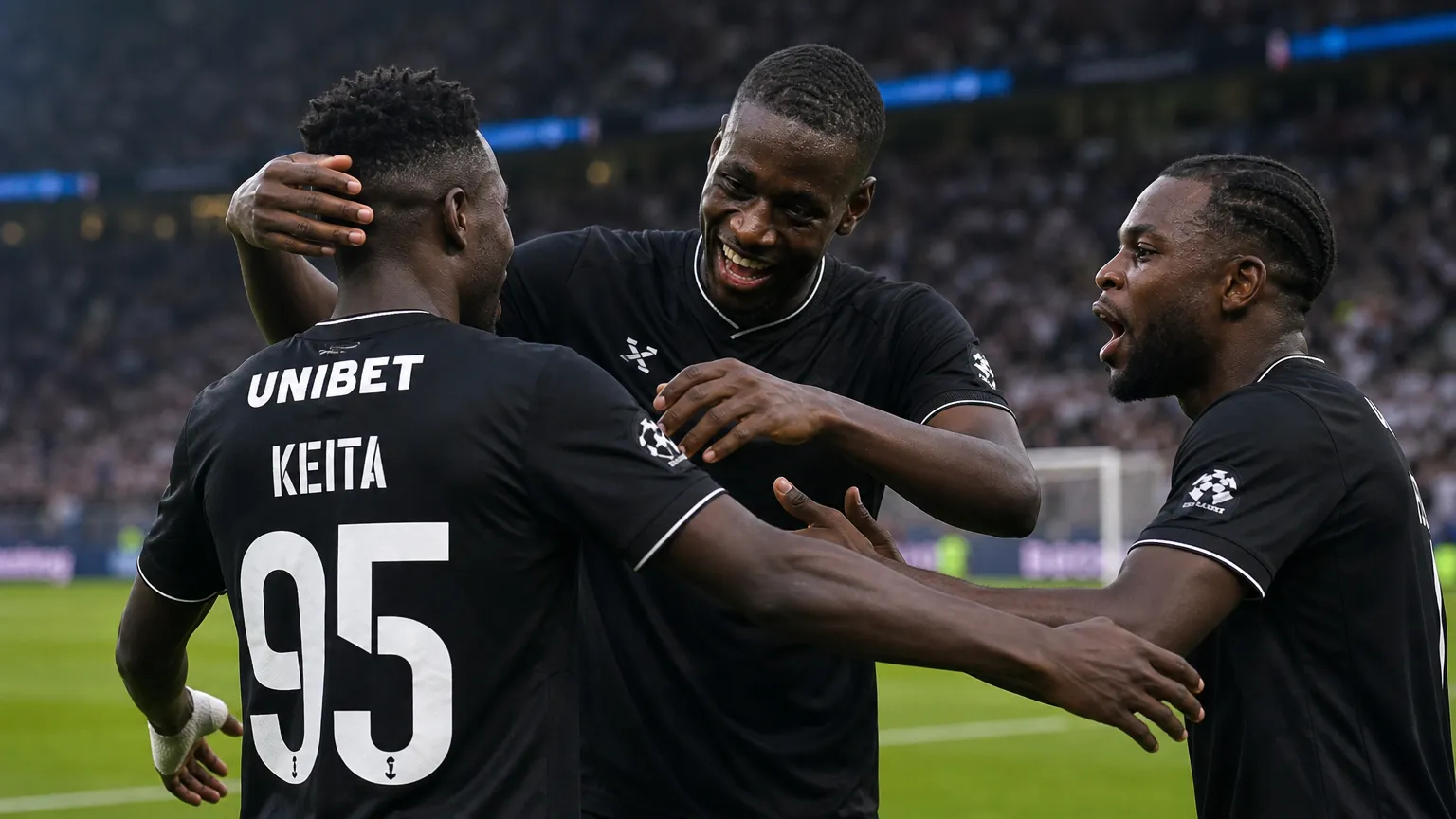 Drie spelers in zwarte wedstrijdtenues vieren samen op het veld.