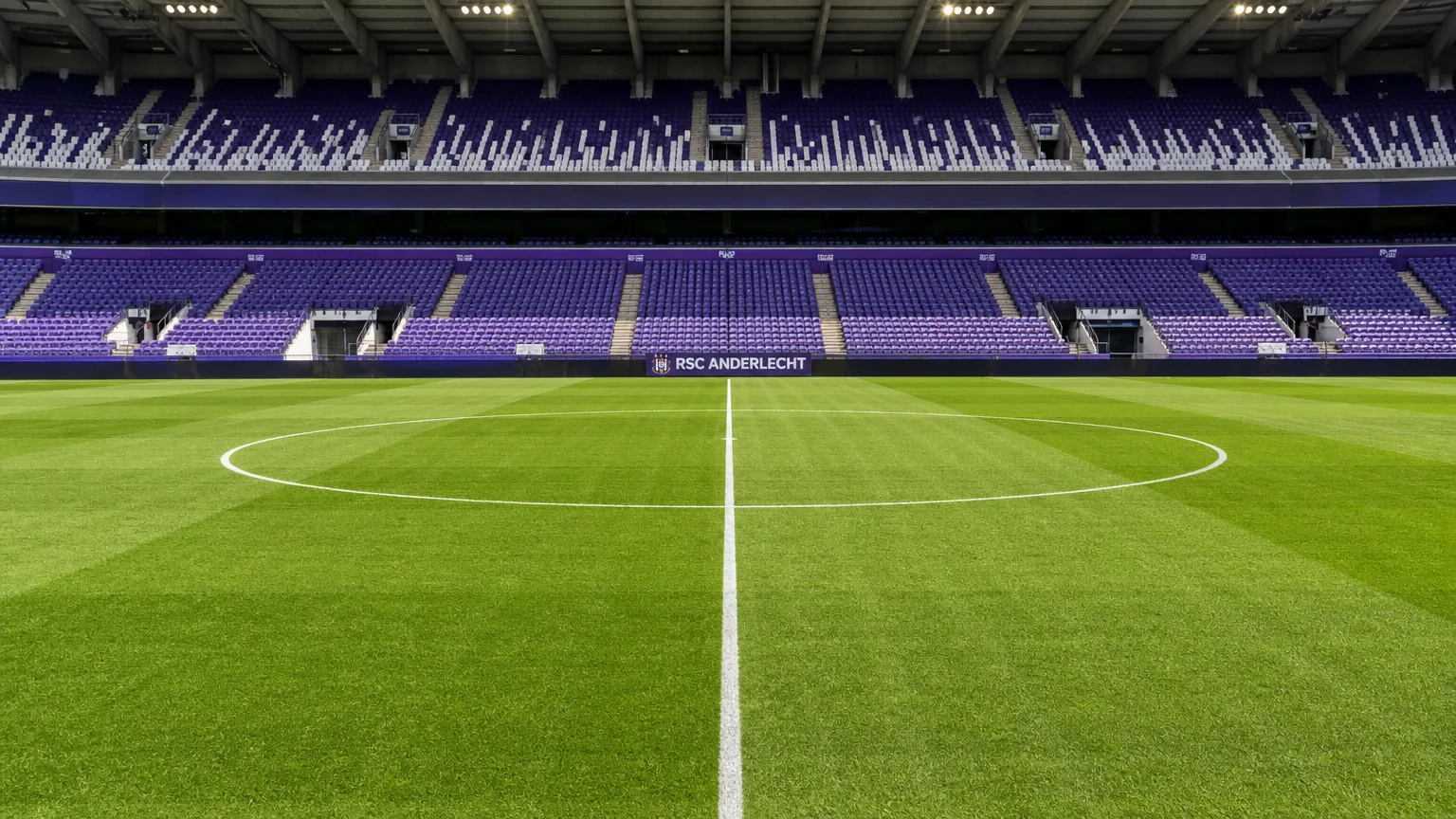 De centrale middenzone van een leeg voetbalveld in een stadion met een discreet Anderlecht-bord.