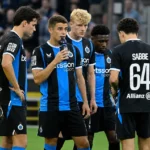 Een groep voetballers in zwart-blauwe tenues tijdens een spelonderbreking naast het veld.