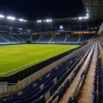Verlicht veld en tribunes in een KAA Gent-stadionomgeving in de avond.