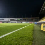 Verlichte zijlijn van een Belgisch voetbalveld met een discreet STVV-bord.