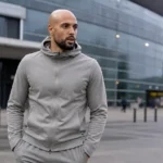 Sofyan Amrabat in neutrale reiskleding buiten een modern voetbalstadion