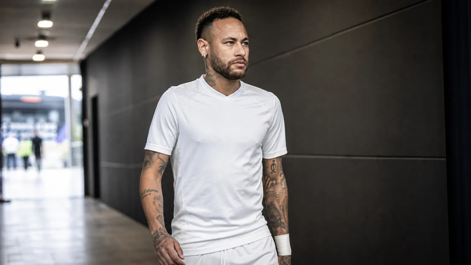 Neymar wandelt in een witte voetbaluitrusting door een stadiongangerij.