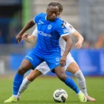 Mujaid Sadick controleert de bal in een blauw wedstrijdtenue.