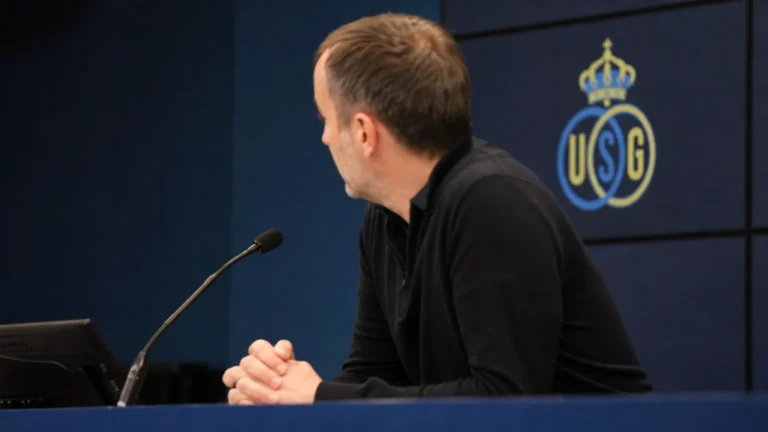 Een niet-herkenbare coach spreekt in een persruimte met een discreet Union-logo op de achtergrond.