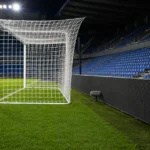 Verlicht doelgebied in een KRC Genk-omgeving met een subtiel clubbord naast het veld.