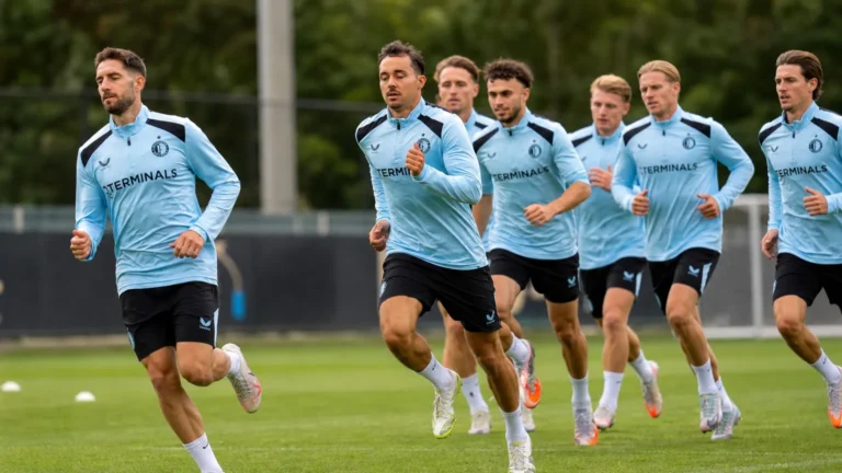 Een groep voetballers in lichtblauwe trainingskleding tijdens een loopoefening.