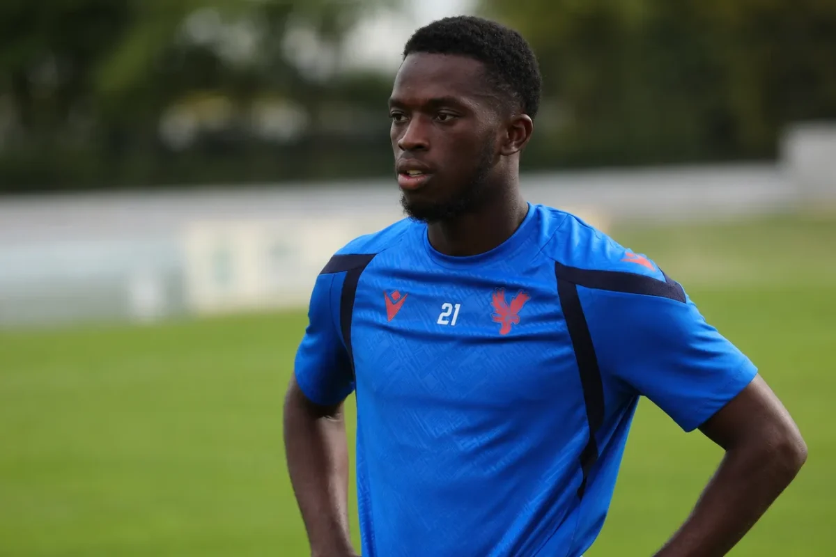 Romain Esse in een blauw voetbaltenue naast een grasveld.
