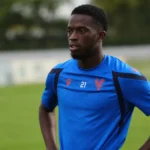 Romain Esse in een blauw voetbaltenue naast een grasveld.