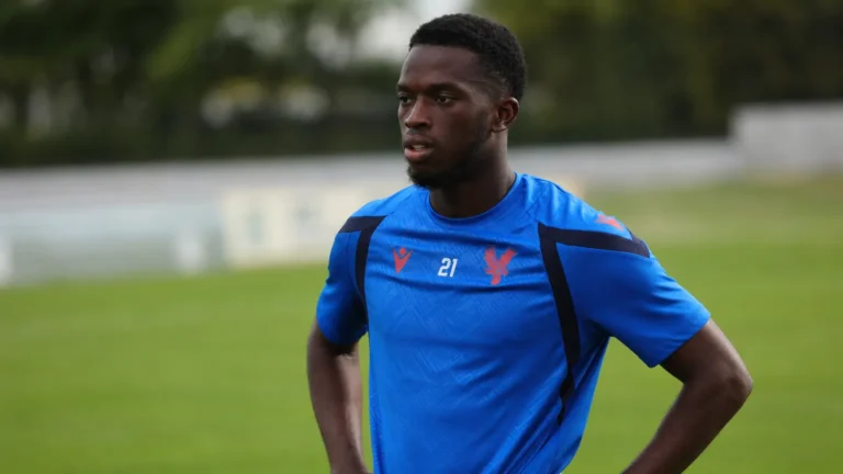 Romain Esse in een blauw voetbaltenue naast een grasveld.